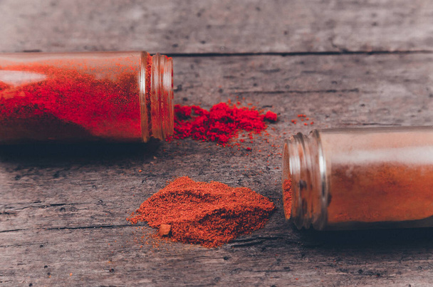 Chilli colorful powder spices scattered from bottle on wooden background - Фото, зображення