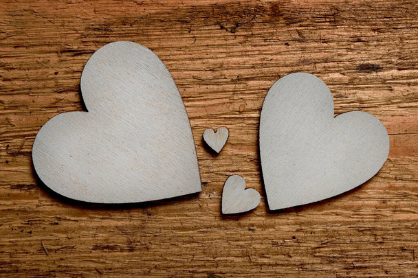 Dwa duże srebrne drewniane serca, dwa małe serca między nimi na drewnianym tle. Symbol dwojga rodziców i dwójki dzieci. - Zdjęcie, obraz
