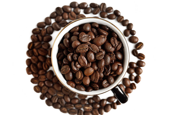 Grãos de café em uma xícara de linho dourado e grãos de café derramados ao redor. Vista superior, fundo branco. Café e porcelana
. - Foto, Imagem