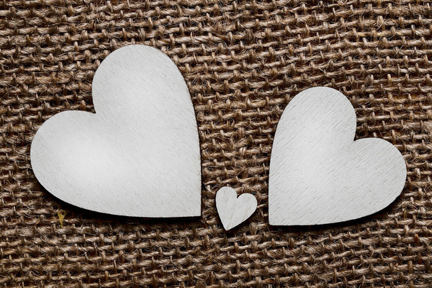 Zwei große silberne Holzherzen und ein kleines Herz dazwischen auf braunem Stoffhintergrund. Symbol für zwei Eltern und ein Kind. - Foto, Bild