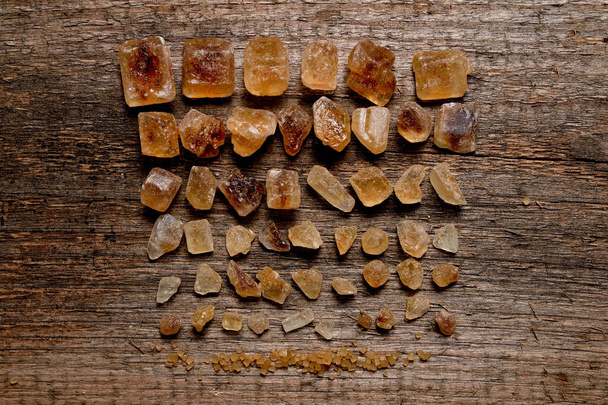 Cristales de azúcar ámbar marrón ordenados por tamaño en tablero de madera viejo
. - Foto, Imagen