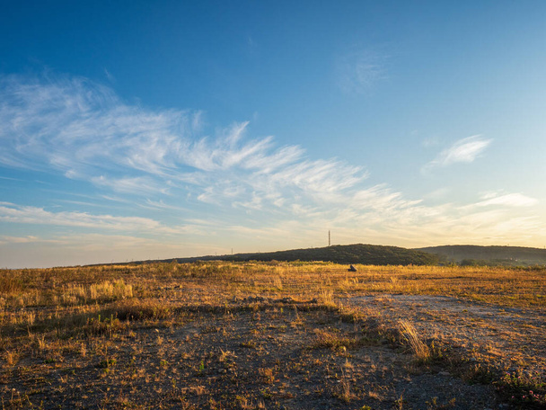 Herfstlandschap. Hoge blauwe lucht met wolken op een verlaten open plek bedekt met wilde vergeelde grassen. Op de verre heuvel is er een TV toren - Foto, afbeelding