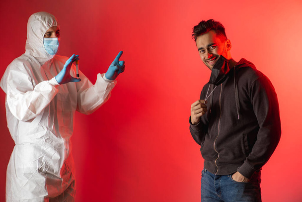 Virologe zeigt einem Mann mit schwarzer Maske das Ergebnis eines Tests auf das Virus, das er negativ, gefährlich, Virus, Sorge, Erfahrung, Schutz, auf rotem Hintergrund ist  - Foto, Bild