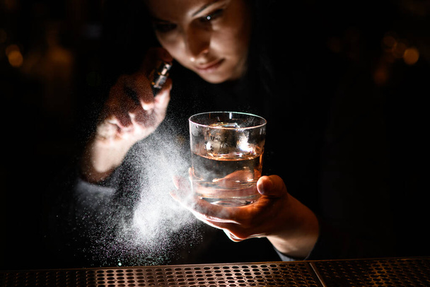 woman holds with one hand glass with drink and spray on it. - Фото, изображение