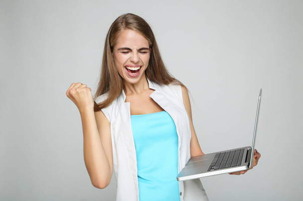 Kaunis nainen käyttää kannettavaa tietokonetta harmaalla taustalla - Valokuva, kuva