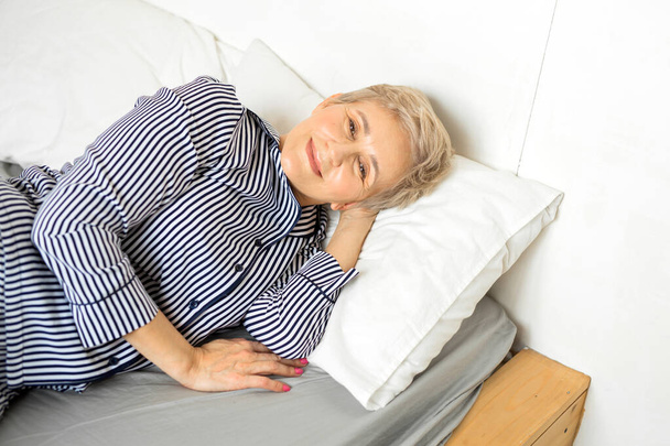 beautiful elderly woman in pajamas lies on the bed - Fotoğraf, Görsel