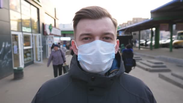 Il tizio che indossa una maschera protettiva dal virus all'aperto tra la gente affollata. Ritratto di giovane uomo con maschera medica si trova in strada. Concetto di salute e sicurezza vita da pandemia di coronavirus - Filmati, video