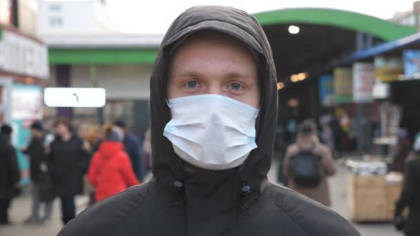 Tıbbi maskeli genç adamın portresi şehir caddesinde duruyor. Dışarıdaki kalabalığın içinde virüsten koruyucu maske takan adam. Coronavirüs salgınından sağIık ve güvenlik kavramı - Video, Çekim