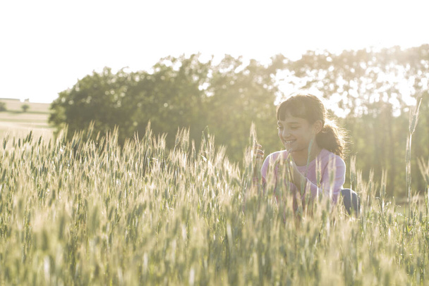 Hnědovlasá holčička s růžovým svetrem na hřišti s bodci a sluncem na zádech. - Fotografie, Obrázek