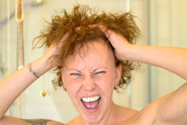 Frusztrált nő, akinek rossz a haja, miközben a kezét a rakoncátlan, göndör hajába dugja, és közelről fejbe lövi. - Fotó, kép