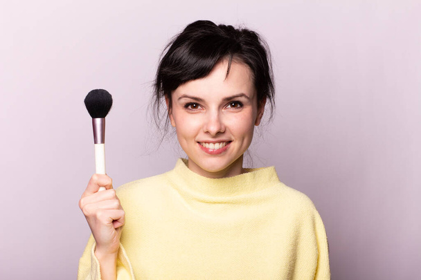 attractive girl in a yellow sweater does makeup with a brush - Photo, image