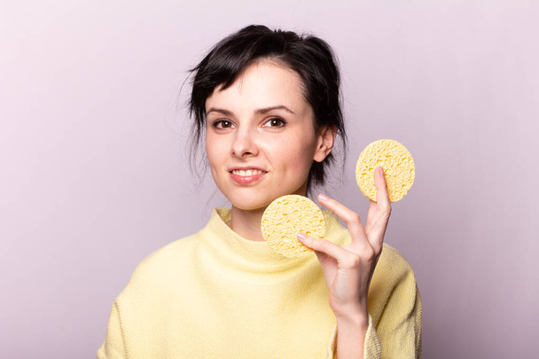 beautiful girl in a yellow sweater holds a sponge in her hands - Foto, Imagen