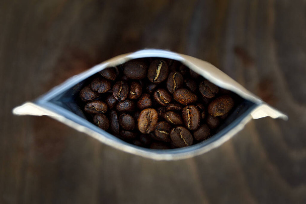 Papper le café dans un sac par le haut avec des grains de café torréfiés foncés. Fond flou en bois foncé
.  - Photo, image