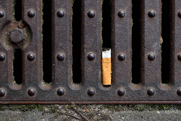 Cigarette butt in a rusty sewer grid, city enviroment. - Φωτογραφία, εικόνα