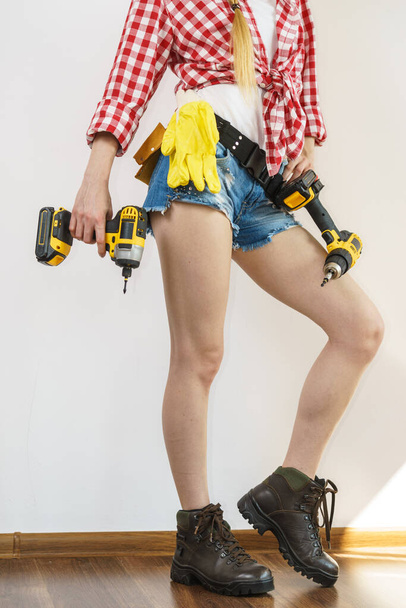 Woman wearing protective workwear toolbelt using drill. Girl working at flat remodeling. Building, repair and renovation. - Zdjęcie, obraz