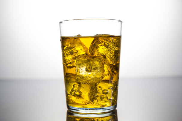 a glass of yellow drink with ice cubes - Foto, afbeelding