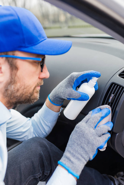 Professional worker using disinfectant and microfiber cloth to clean car interior. - Photo, image