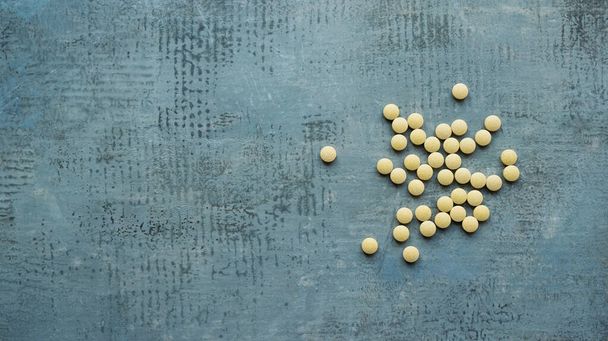 žluté kulaté tablety nebo pilulky vitamíny ploché ležel na modrém kamenném betonovém stole, shora dolů pohled, horizontální stock fotografie zátiší pozadí s kopírovacím prostorem - Fotografie, Obrázek