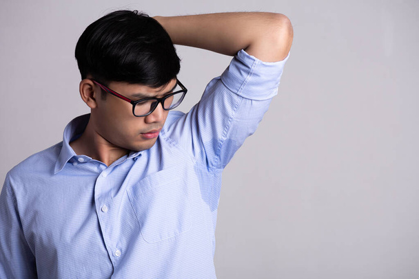 Nahaufnahme asiatischer Mann mit Hyperhidrose schwitzend. Junger asiatischer Mann mit Schweißflecken auf der Kleidung vor grauem Hintergrund. Gesundheitskonzept. - Foto, Bild