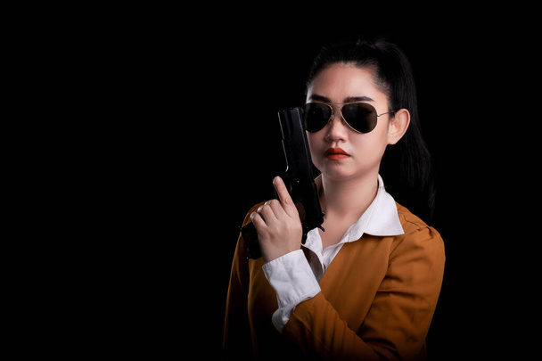 Портрет красивая асеа женщина в желтом костюме одной рукой с пистолетом на черном фоне, молодая сексуальная девушка длинные волосы с пистолетом смотреть в камеру, красивые женщины стоят с пистолетом
 - Фото, изображение