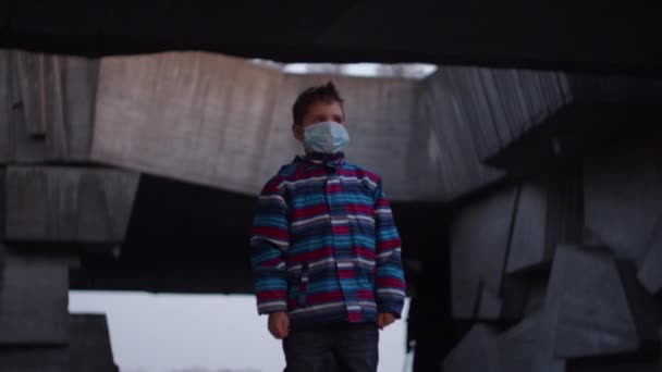 Boy in medical protective mask stands in shelter during pandemic outbreak of coronavirus COVID-19 and watching around. Quarantine national emergency and martial law to combat coronavirus.  - Filmmaterial, Video