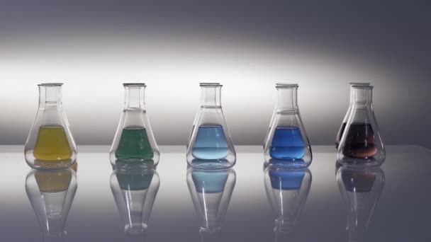 Empty and mixed colour liquid filled erlenmeyer flasks reflecting on table - Footage, Video