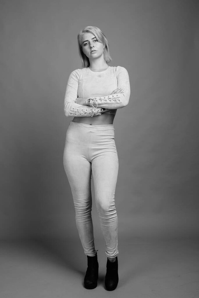 Studioaufnahme einer jungen schönen Rebellin mit kurzen Haaren vor grauem Hintergrund in schwarz-weiß - Foto, Bild