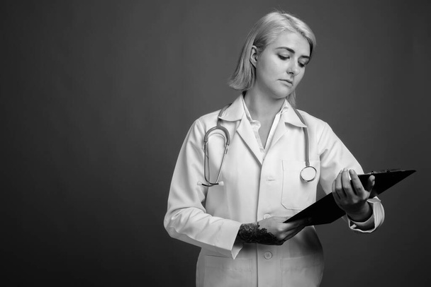 Studio shot της νεαρής όμορφη γυναίκα γιατρός με κοντά μαλλιά σε γκρι φόντο σε μαύρο και άσπρο - Φωτογραφία, εικόνα