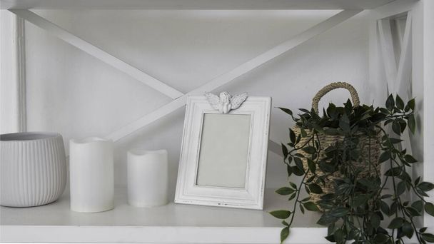 Белая рамка и крытый цветочный горшок и белые свечи и ваза на белой полке
 - Фото, изображение