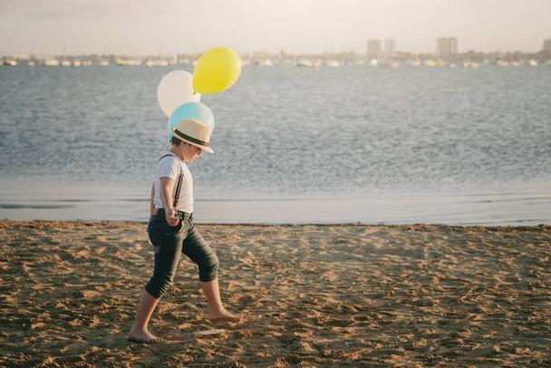 bambino con palloncini colorati passeggiando lungo la spiaggia
  - Foto, immagini
