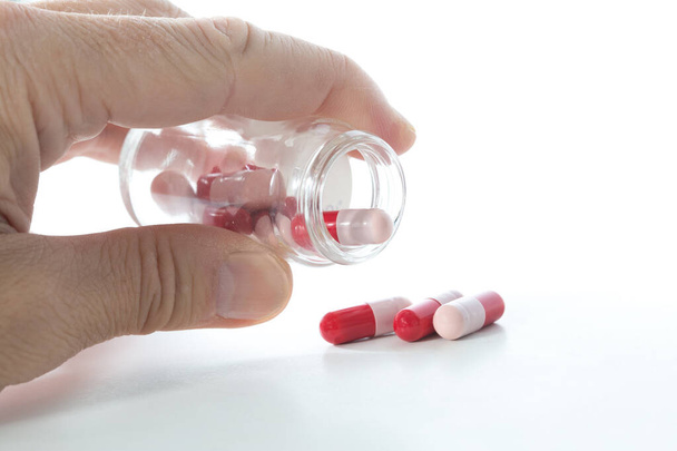 Man takes red and pink antibiotics capsule, white background - Photo, Image