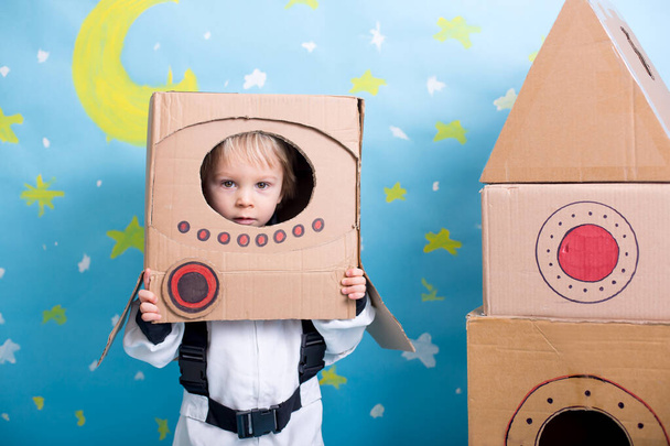 Dulce niño, vestido de astronauta, jugando en casa con cohete de cartón y casco hecho a mano de caja - Foto, Imagen