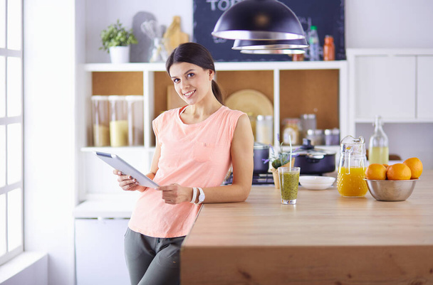 Beautiful young woman using a digital tablet in the kitchen - 写真・画像