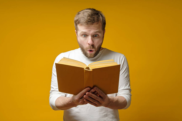 Чоловік в жовтому шарфі, заклятий, читає цікаву книгу і здивований тим, що написано. Концепція освіти
. - Фото, зображення