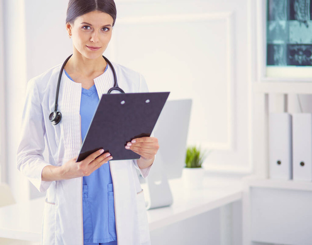 Jeune femme médecin souriante avec stéthoscope tenant un dossier au cabinet des médecins - Photo, image