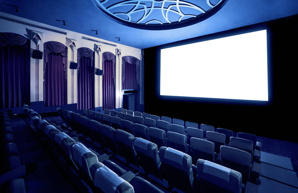 Экран кинотеатра перед рядами сидений в кинотеатре, показывающий белый экран, проецируемый от кинематографа. Кинотеатр оформлен в классическом стиле для роскошного просмотра фильмов
. - Фото, изображение