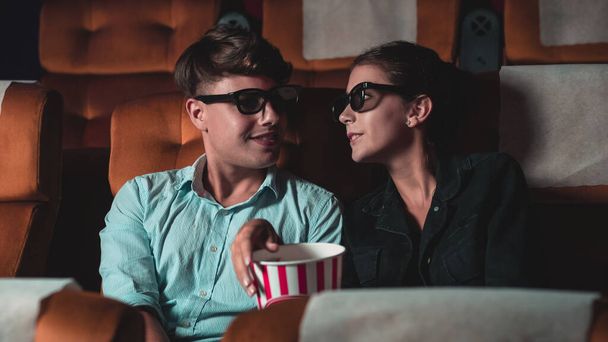 Man and woman in the cinema watching a movie with 3D glasses. with interest looking at the screen, exciting and eating popcorn - Фото, зображення