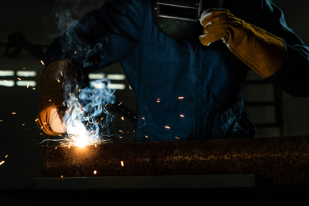 Metal welder working with arc welding machine to weld steel at factory while wearing safety equipment. Metalwork manufacturing and construction maintenance service by manual skill labor concept. - Fotografie, Obrázek