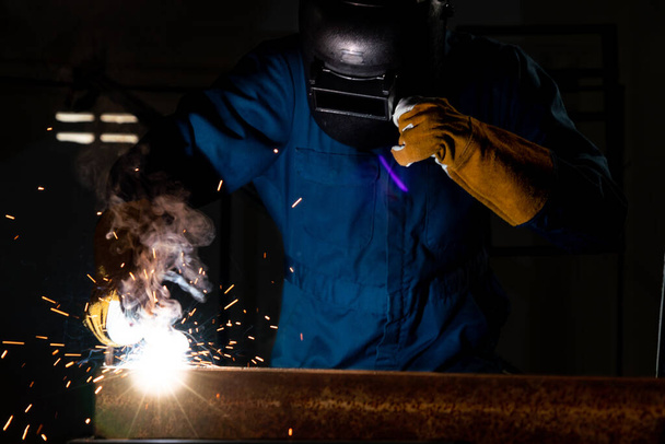 Metal welder working with arc welding machine to weld steel at factory while wearing safety equipment. Metalwork manufacturing and construction maintenance service by manual skill labor concept. - Photo, Image