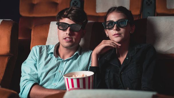 3Dメガネで映画を見ている映画館の男と女。画面を見て興味を持ちポップコーンを食べ - 写真・画像