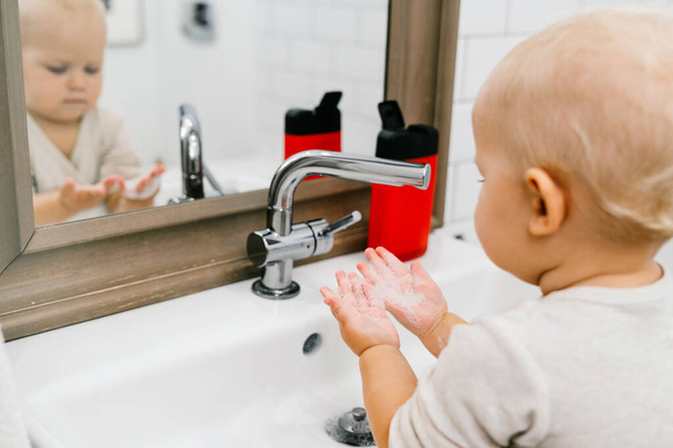 Il bambino si lava indipendentemente le mani in un bagno luminoso con un disinfettante speciale. Prevenzione delle malattie infettive, dell'influenza e del coronavirus
. - Foto, immagini