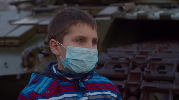 Schooler boy in medical protective mask stands by military machine during pandemic outbreak of coronavirus COVID-19. Quarantine emergency and martial law to combat coronavirus. Close up - Filmmaterial, Video