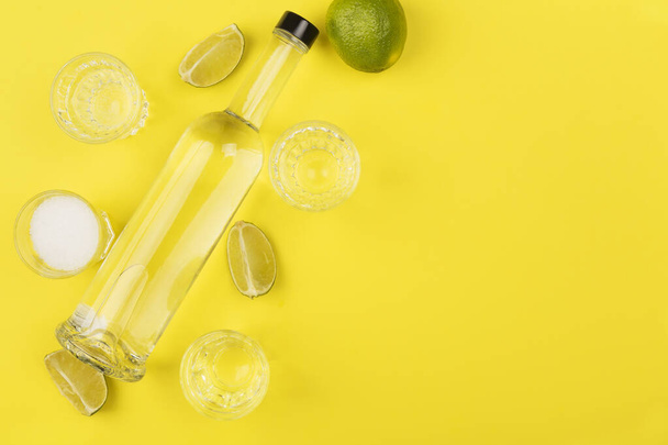 Bottle of tequila, lime, salt, shots on yellow background. Top view, copy space - 写真・画像