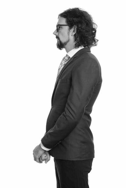 Studio shot of handsome bearded businessman with curly hair in suit isolated against white background in black and white - Photo, Image
