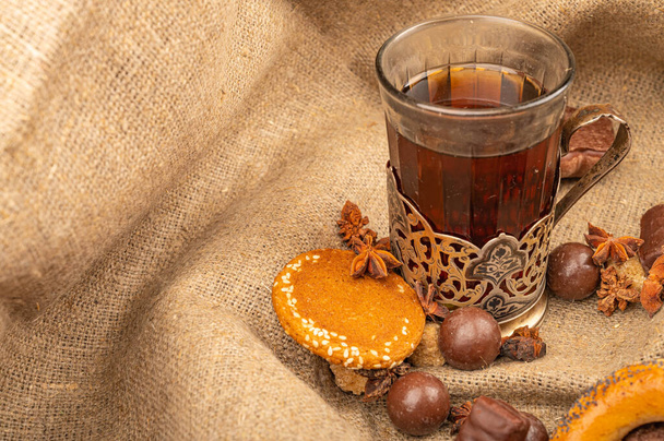 Стакан чая в винтажном держателе для чашки, печенье и шоколад на фоне текстурированной ткани. Закрыть
 - Фото, изображение