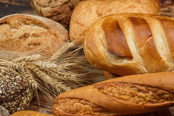 Různé bochníky chutného chleba s pšenicí, moukou a lepkem na dřevěném stole - Fotografie, Obrázek