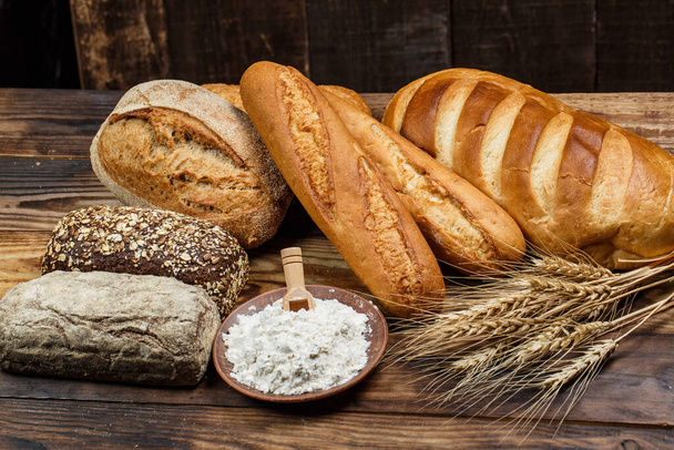 Different loaves of tasty bread with wheat, flour and gluten on a wooden table - Foto, imagen