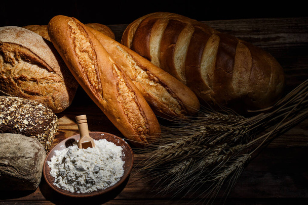 Different loaves of tasty bread with wheat, flour and gluten on a wooden table - Fotoğraf, Görsel