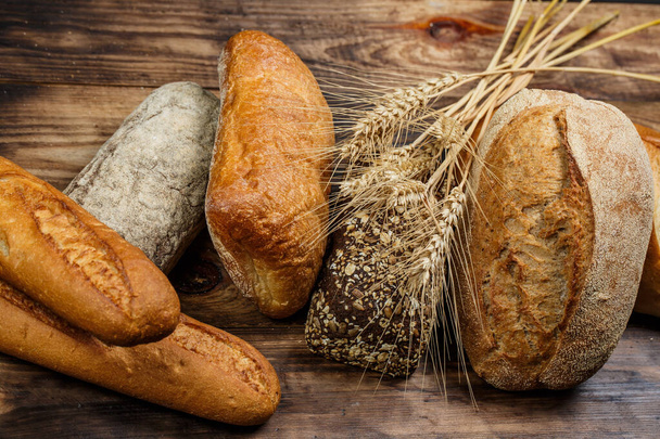 Pães diferentes de pão saboroso com trigo, farinha e glúten em uma mesa de madeira
 - Foto, Imagem