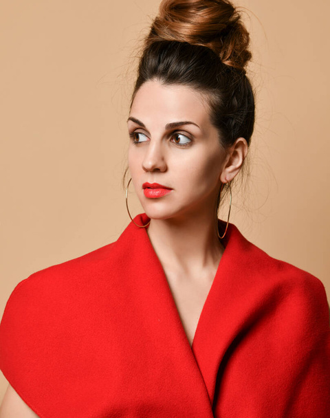 Bruna ragazza con trucco serale, in orecchini e scialle rosso. Sta posando in piedi sullo sfondo dello studio beige. Primo piano
 - Foto, immagini